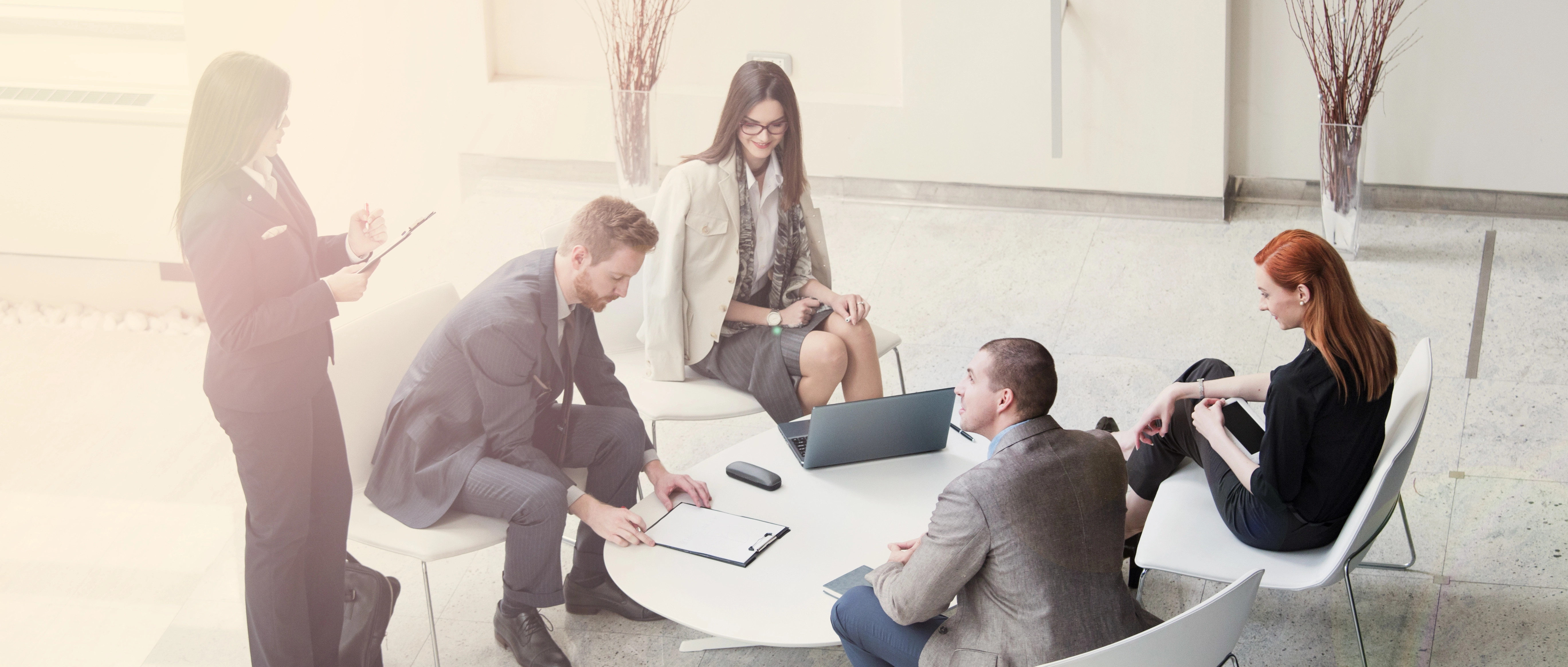 A Group of Five Professionals Sitting and Standing Around a Table Meeting